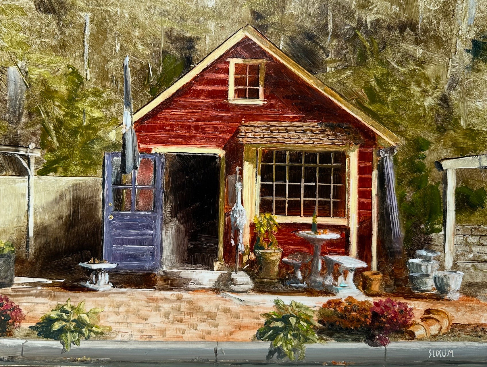 Small red wooden shed with a window, door open, surrounded by plants and outdoor furniture, against a rocky background.