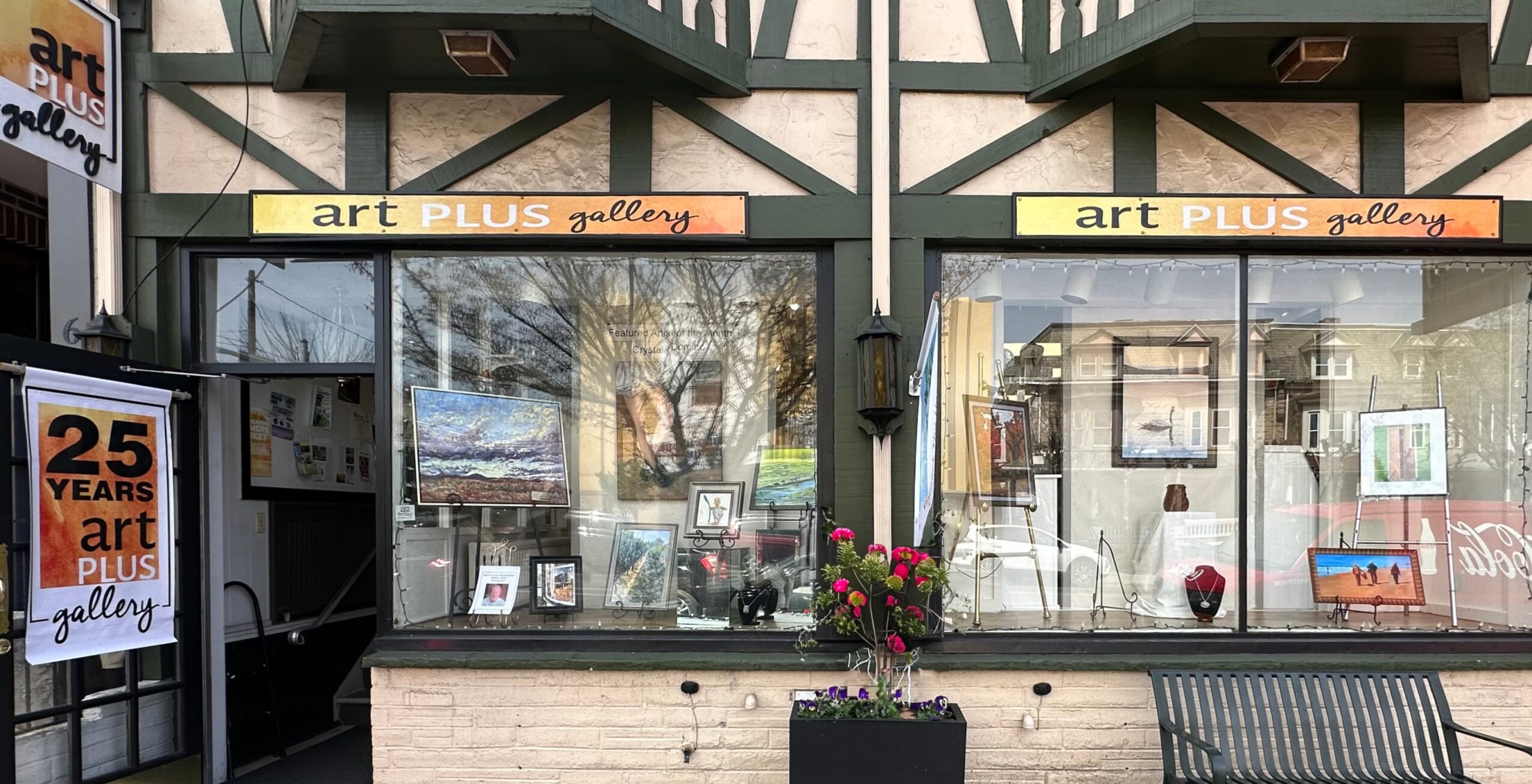 Art gallery storefront with large windows displaying artwork and a sign reading 'art PLUS gallery'.