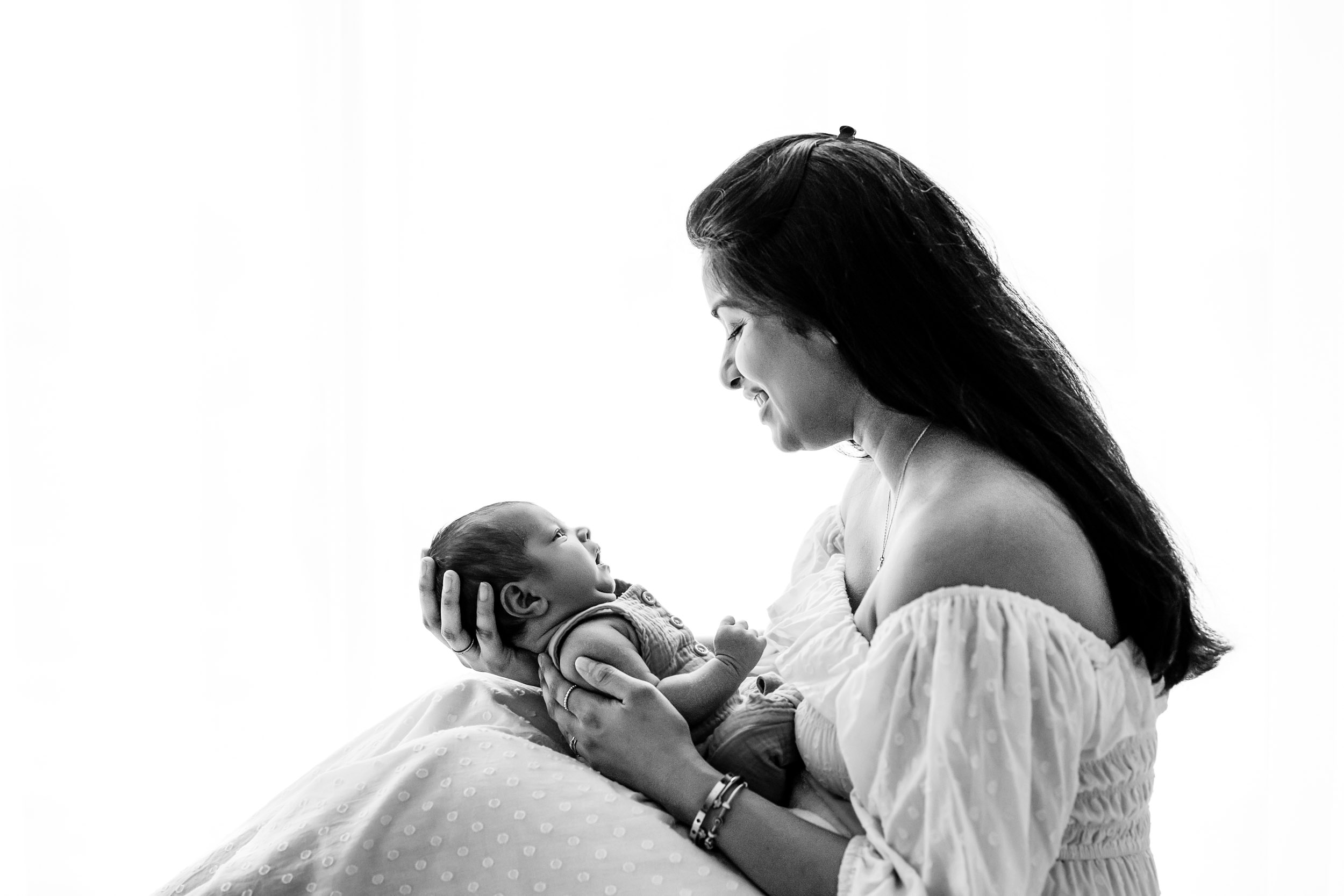Woman holding a baby, both smiling, in a bright setting, with the woman looking at the baby.