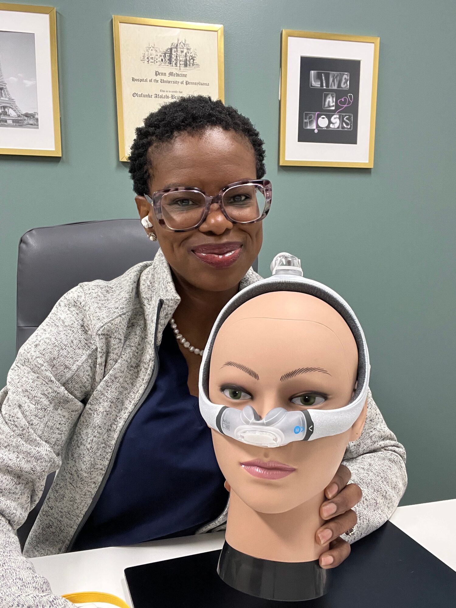 Two women, one wearing glasses and the other with a nasal oxygen tube, sit together in an office setting.