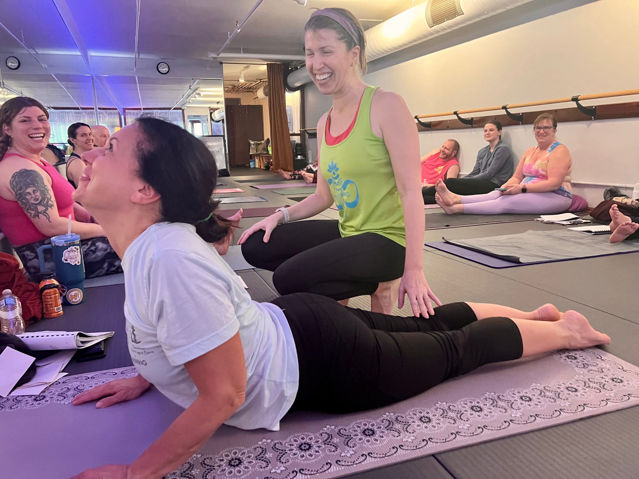 Group of women practicing yoga in a studio, with one woman smiling and another lying on a mat.