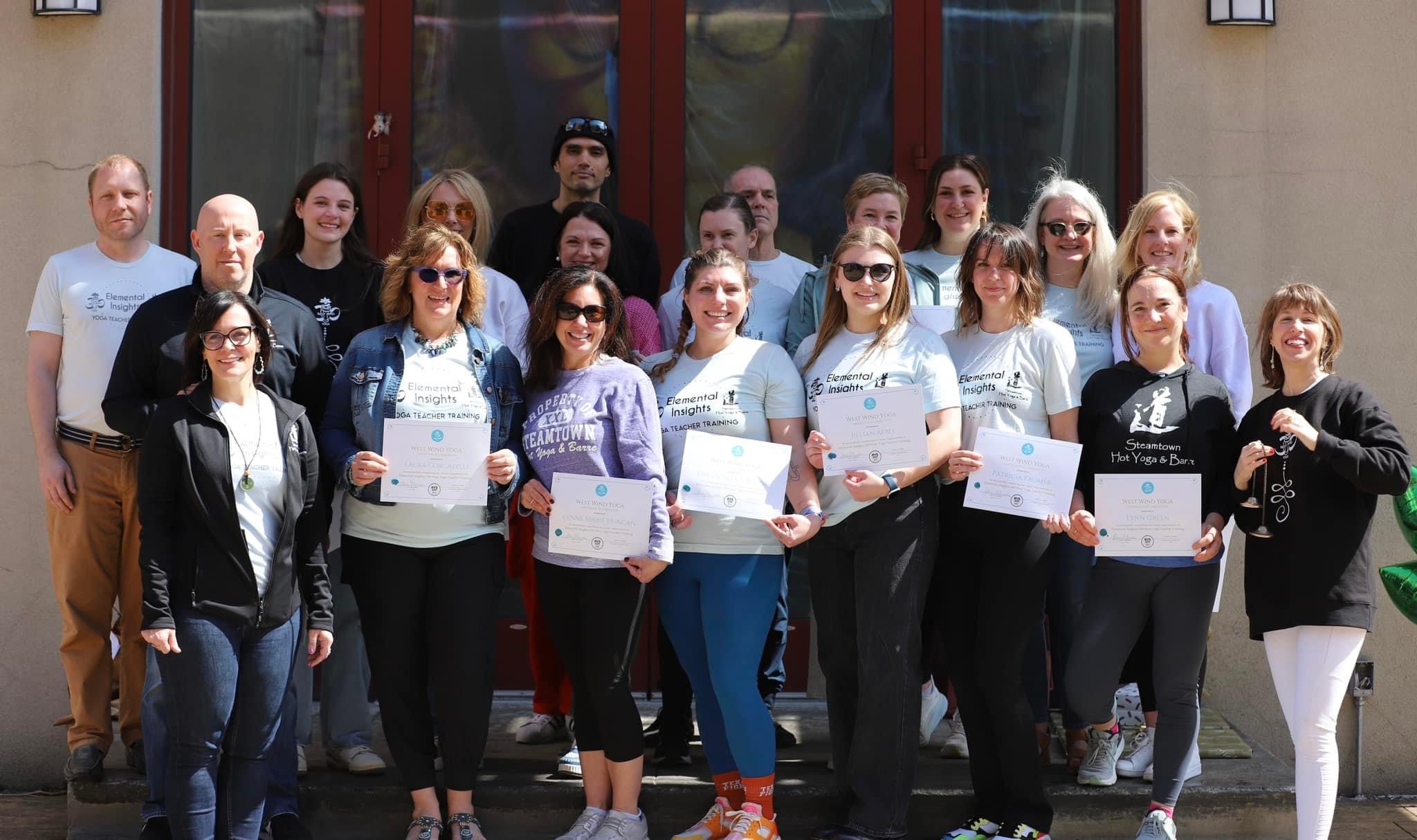 Group of people standing outside a building, holding certificates, smiling, with some wearing sunglasses.
