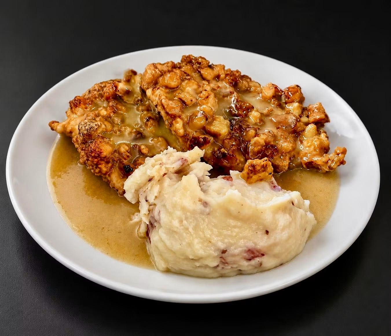 Plate with fried chicken, mashed potatoes, and gravy on a black background.