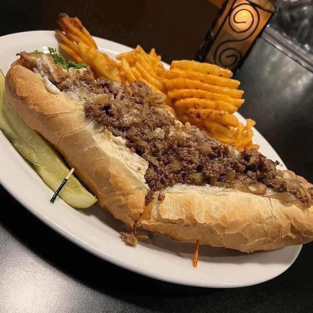 Submarine sandwich with ground beef, lettuce, and lemon wedge, served with waffle fries on a white plate.