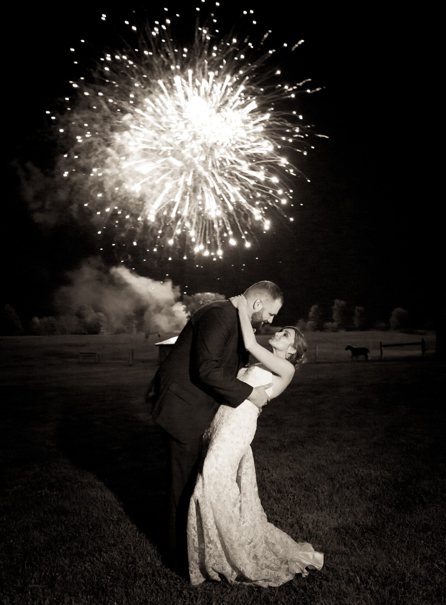 A couple dancing outdoors at night with fireworks in the sky behind them, celebrating a special occasion.