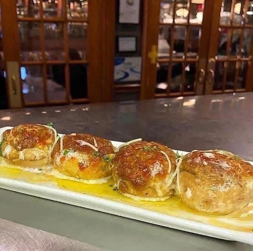Four baked bread rolls on a white plate with sauce, in front of a wooden restaurant interior.