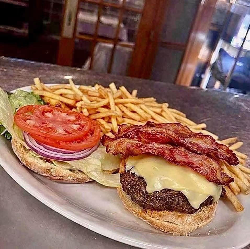 Hamburger with lettuce, tomato, onion, cheese, bacon, and fries on a plate.