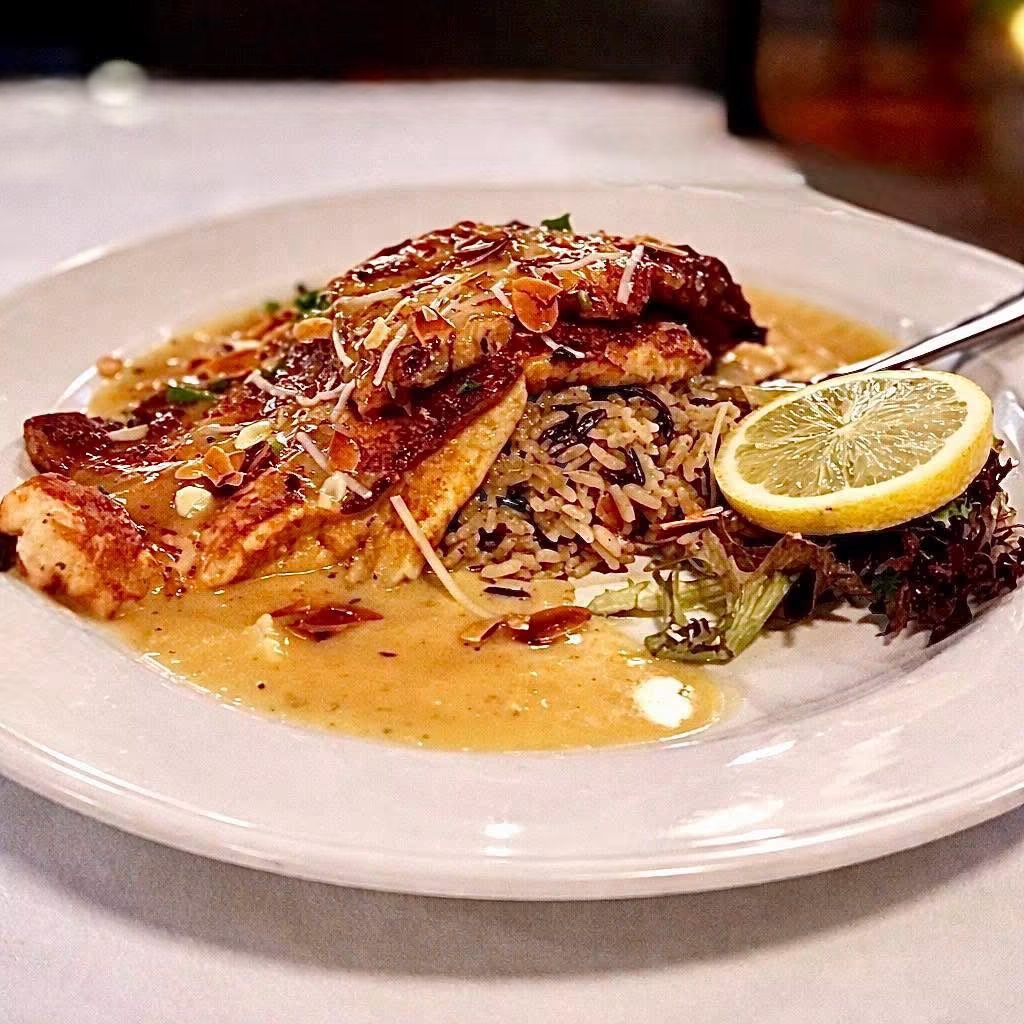 Plate with grilled fish, rice, lemon wedge, and sauce, garnished with herbs on a white plate.