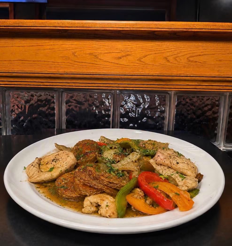 Plate of grilled chicken, bell peppers, and vegetables on a white dish, with a wooden and glass brick background.