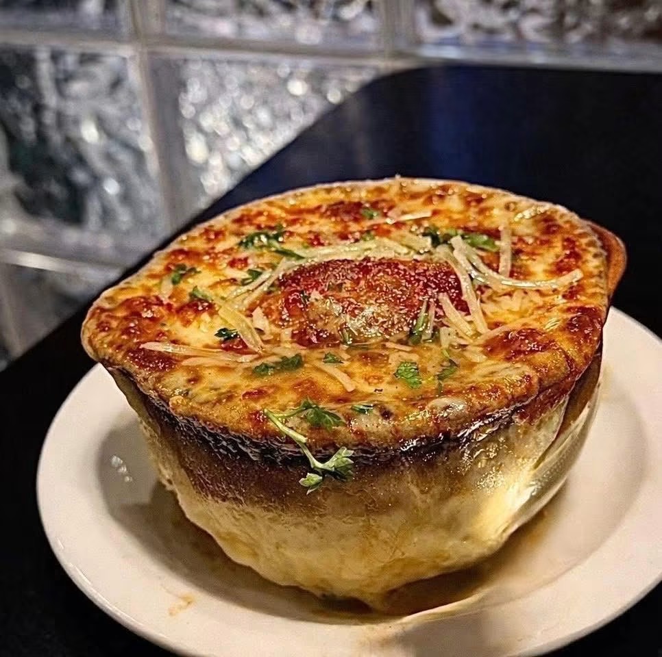 Baked dish with cheese, vegetables, and a slice of tomato on top, served in a bowl on a white plate.