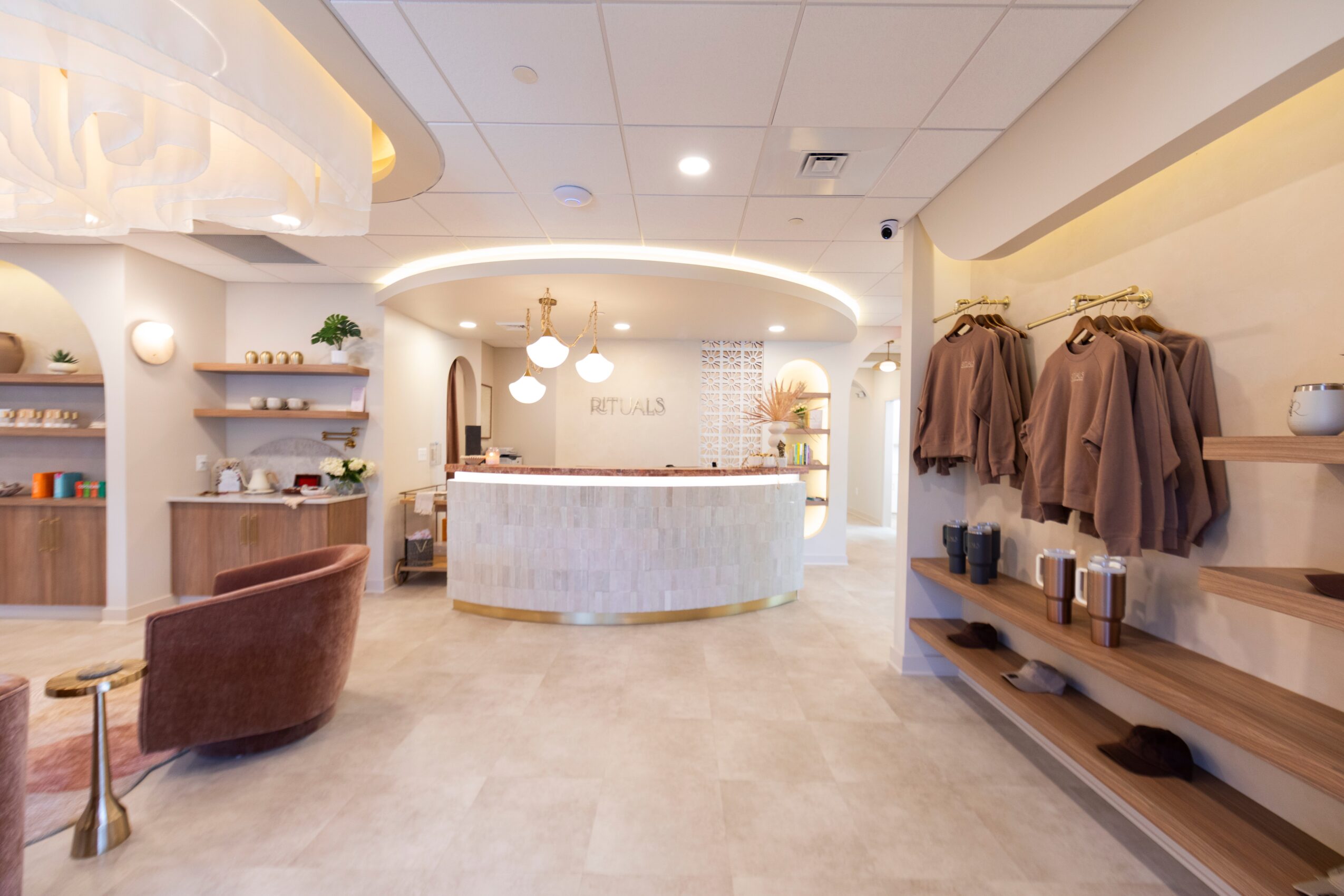 Interior of a modern retail store with a curved reception desk, clothing on shelves, and seating area, well-lit and spacious.