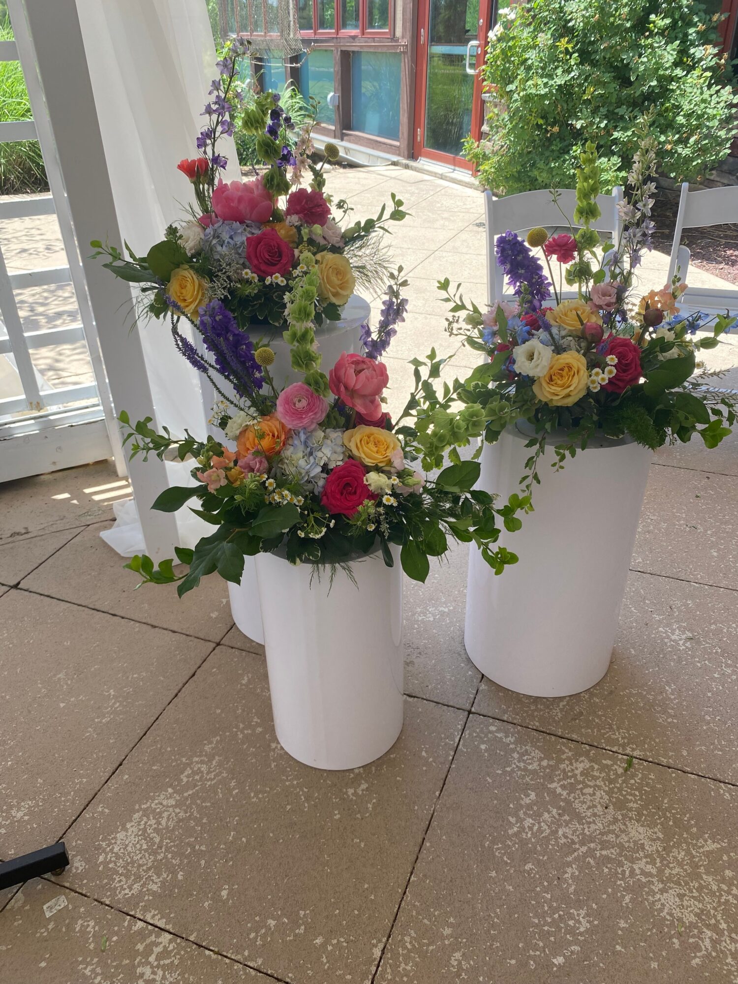 Three white vases with colorful flower arrangements on a tiled floor near a window.