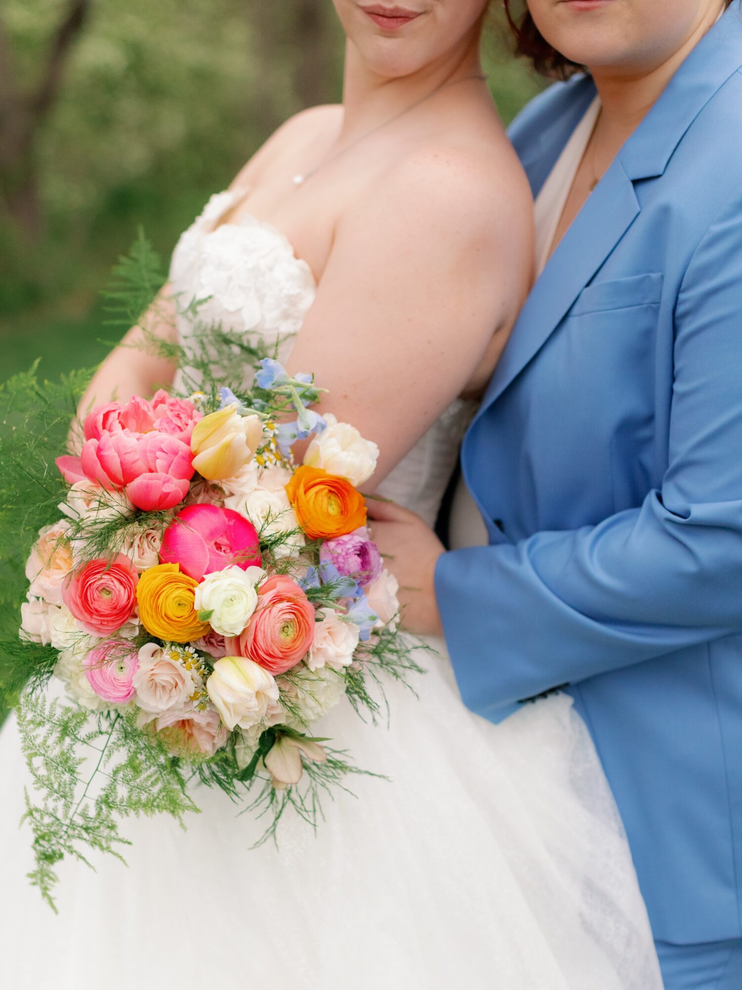Two people, one in a wedding dress holding a colorful bouquet, the other in a blue suit, outdoors.