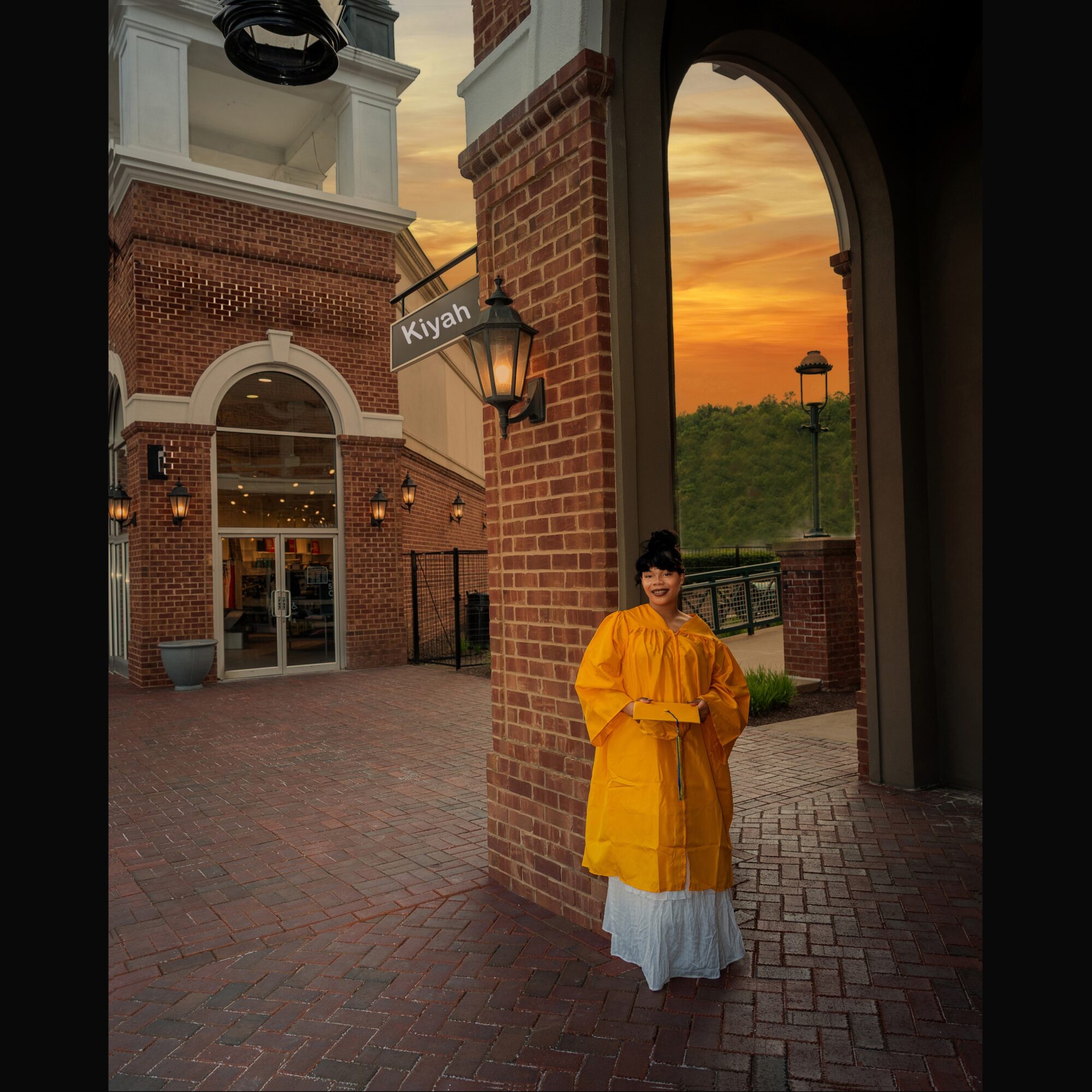 Person in yellow raincoat standing outside brick building during sunset, with a scenic view of the sky and greenery.