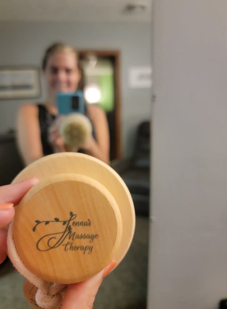 Person taking a mirror selfie holding a massage therapy product, with a blurred background, in a room with framed pictures.