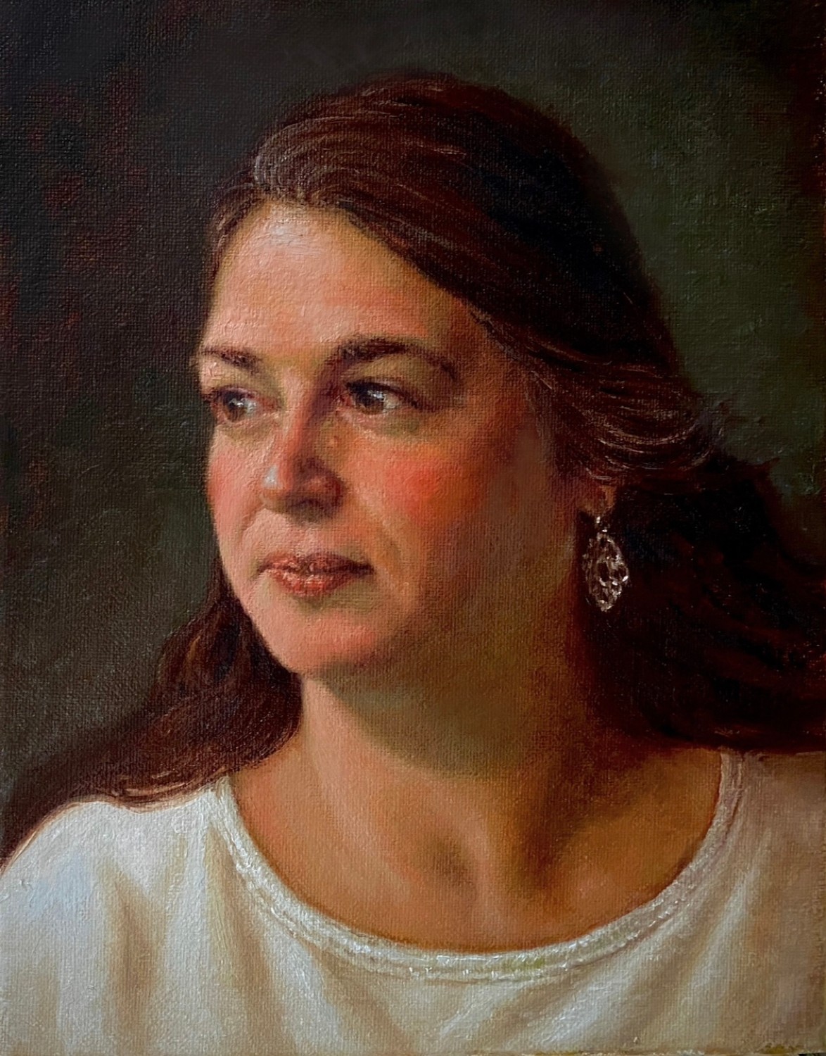 Portrait of a woman with long brown hair, wearing earrings and a white top, looking to the side.