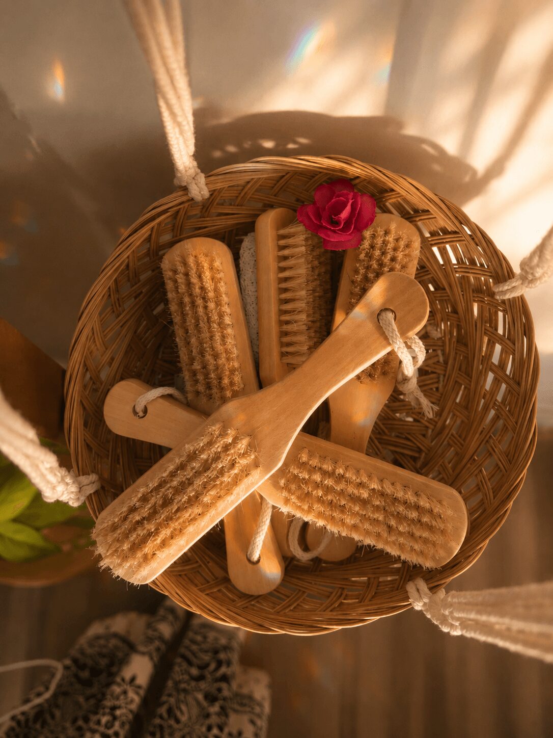 Basket containing cookies, a pink rose, and a wooden spoon, viewed from above, with sunlight creating rainbow reflections.