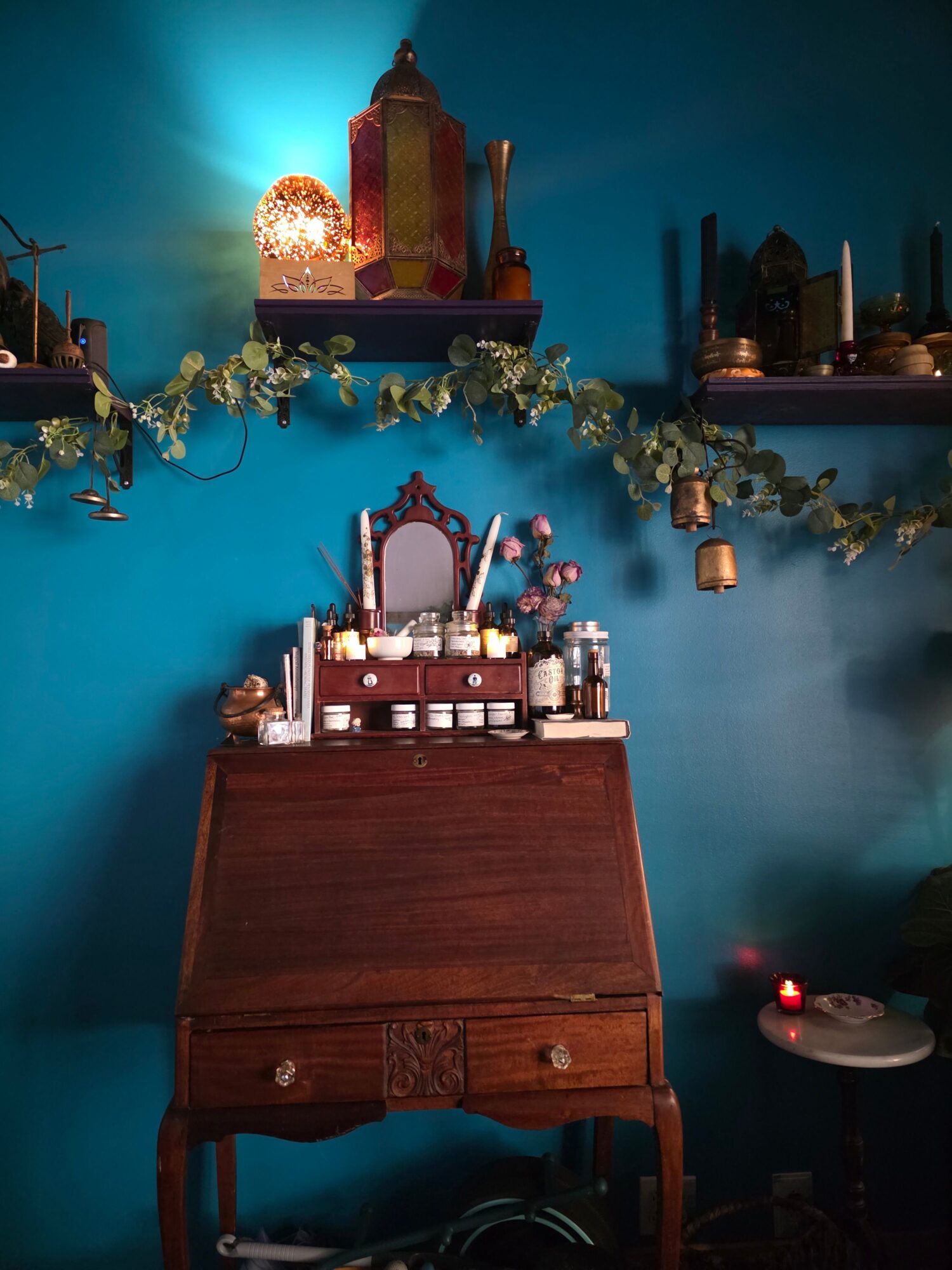 A wooden cabinet with bottles and glassware, decorated with greenery and candles, against a blue wall with shelves and ornaments.