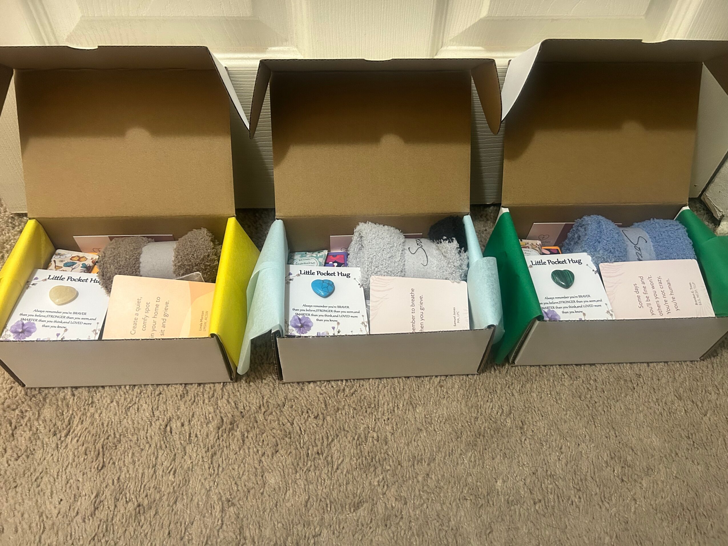 Four open boxes containing socks arranged in color groups on a carpeted surface.