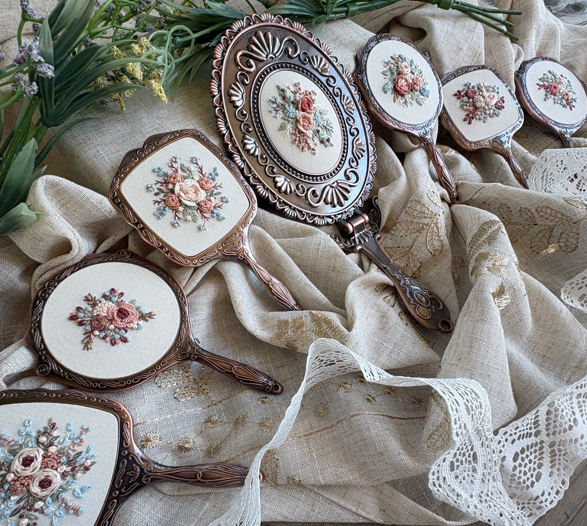 Vintage hand mirrors and a decorative tray with floral embroidery, arranged on fabric with lace details.