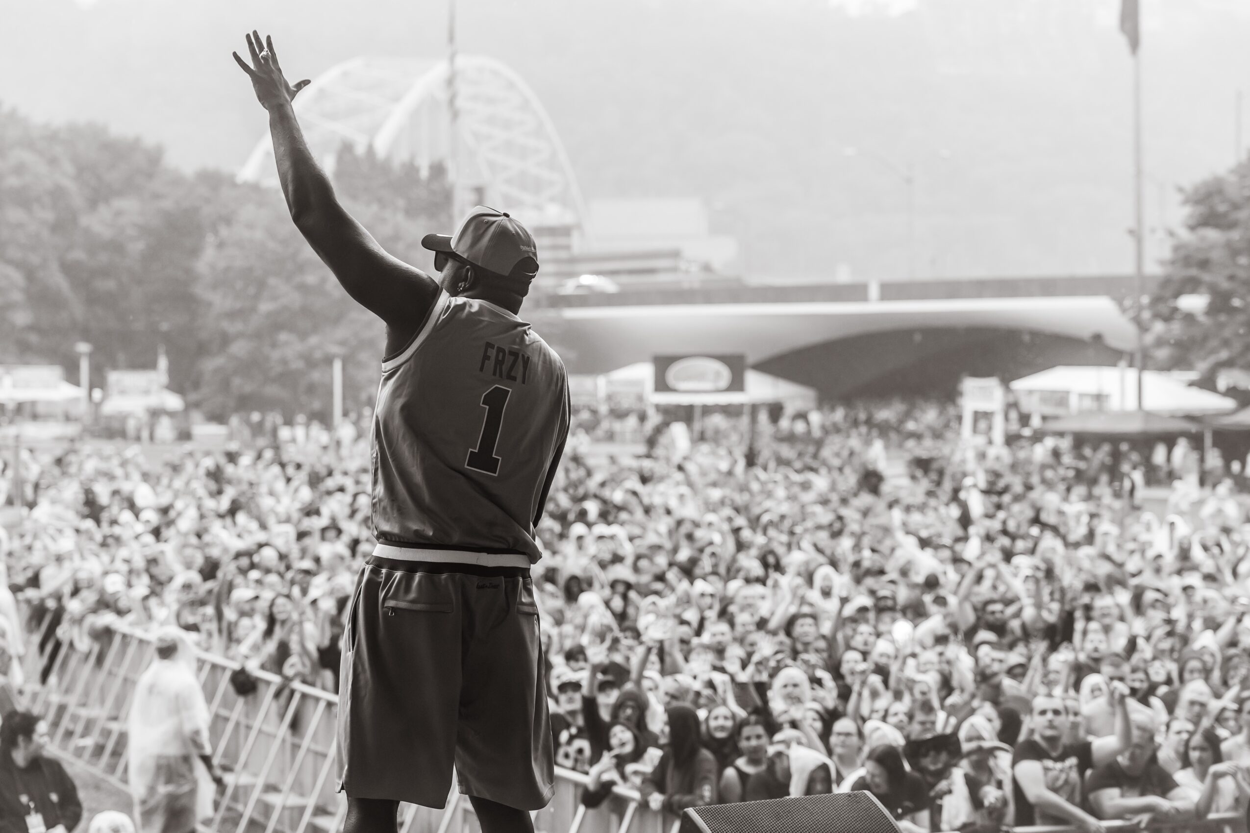 Basketball player waving to crowd during game, large audience in background, outdoor setting, black and white photo.