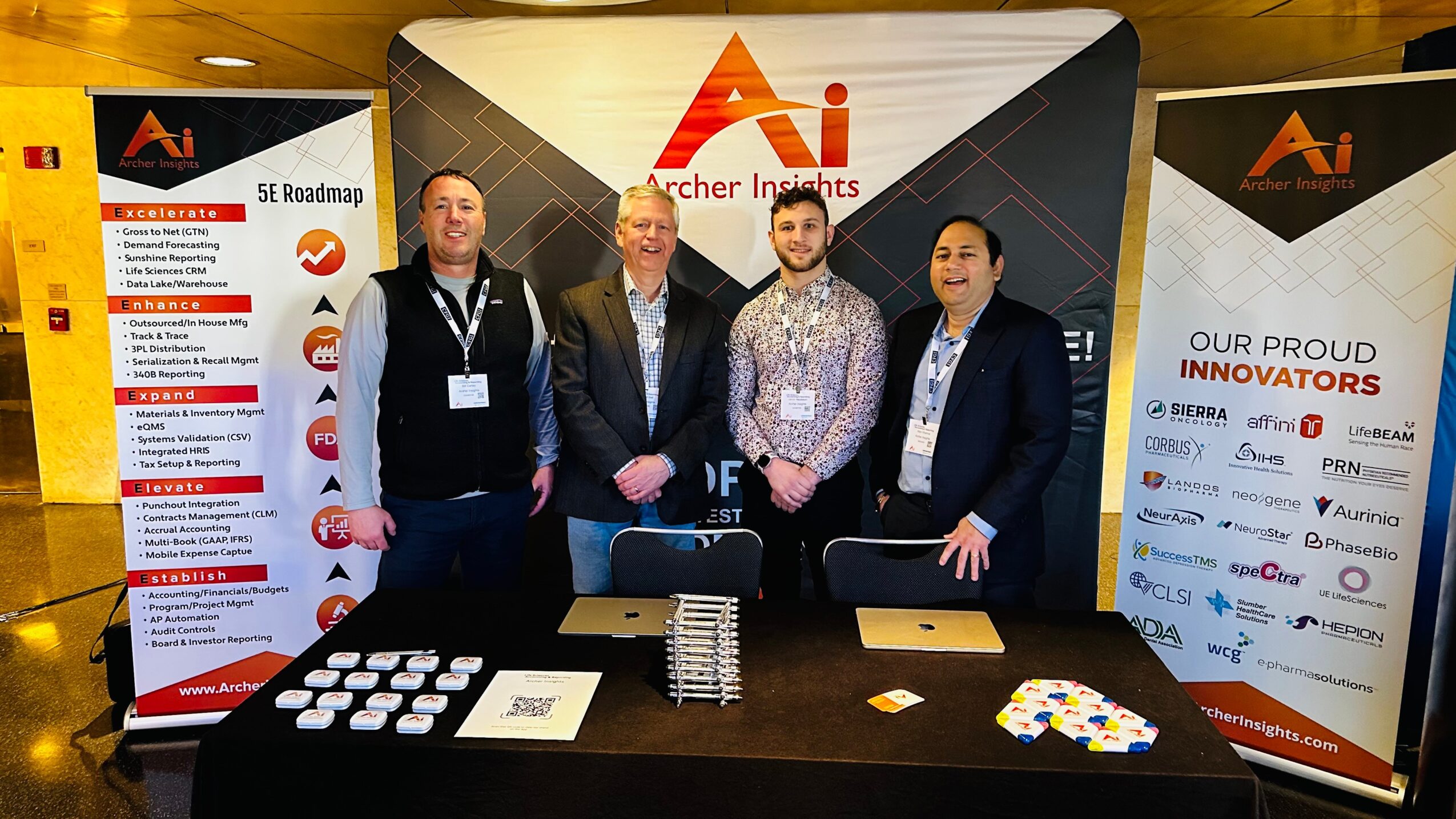 Four men stand behind a table at a conference booth with AI Research Insights banners, smiling and facing forward.