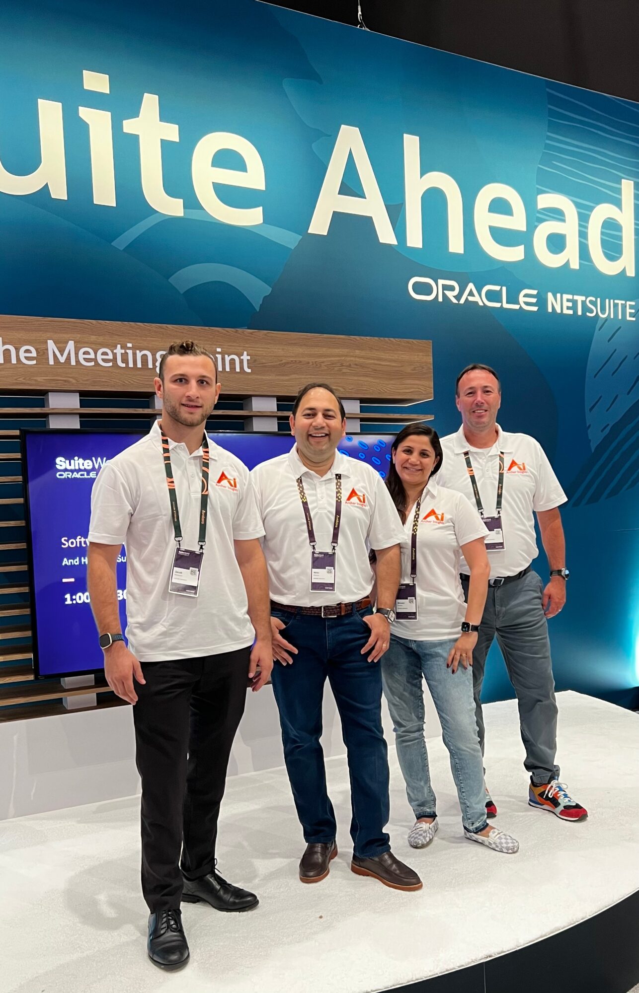 Four people standing in front of a large blue display with text, smiling, at a conference or event.