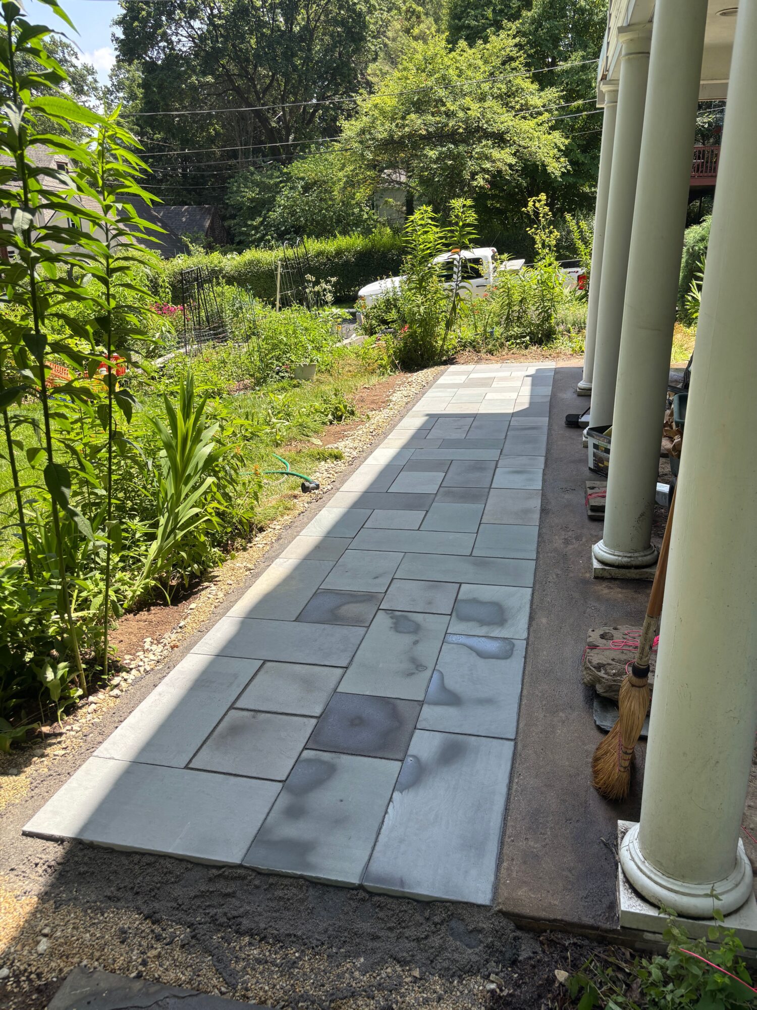 Newly laid gray paving stones on a garden pathway with greenery and trees in the background.
