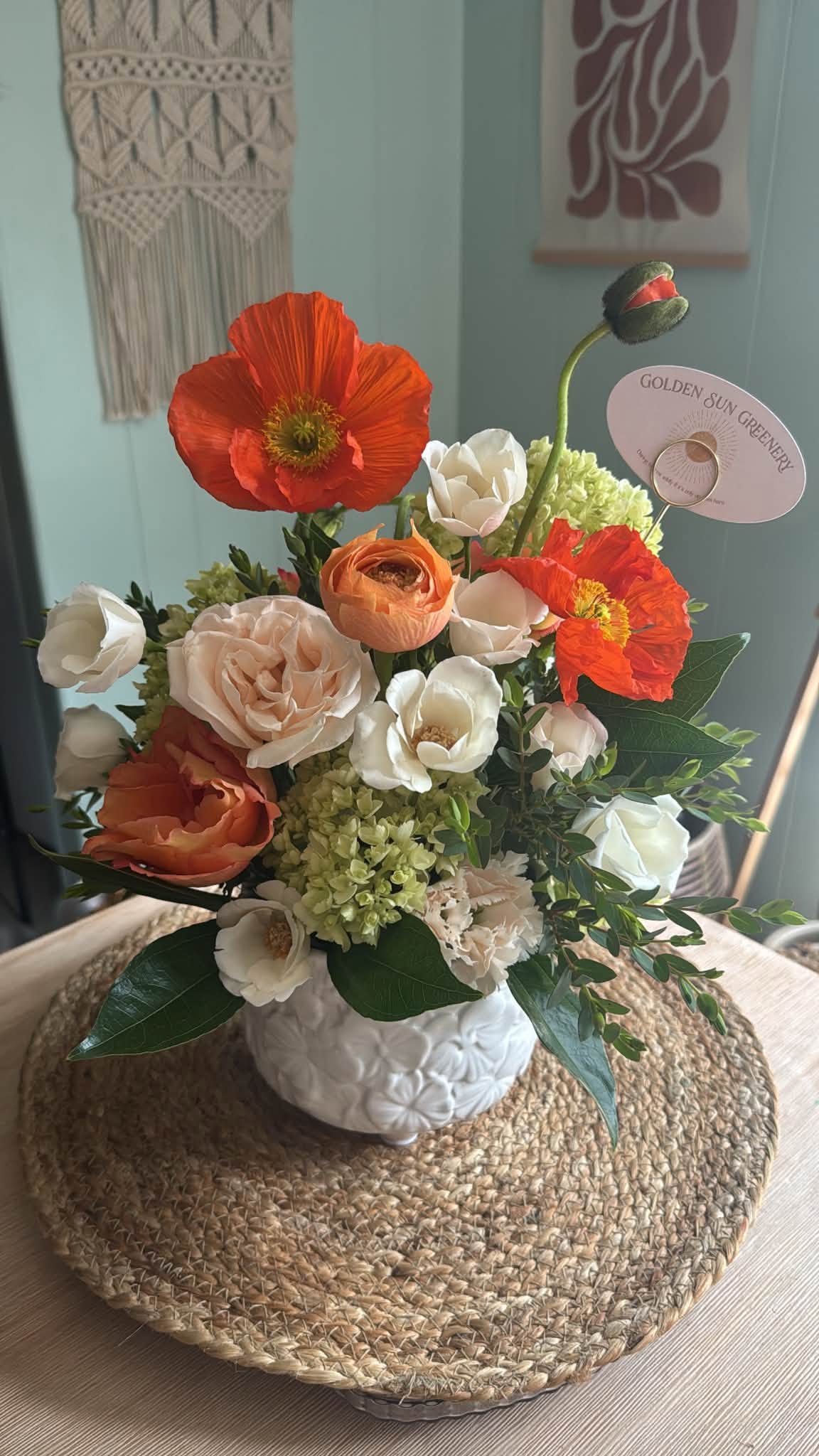 Flower arrangement with orange, white, and peach blooms in a white textured vase on a woven mat.