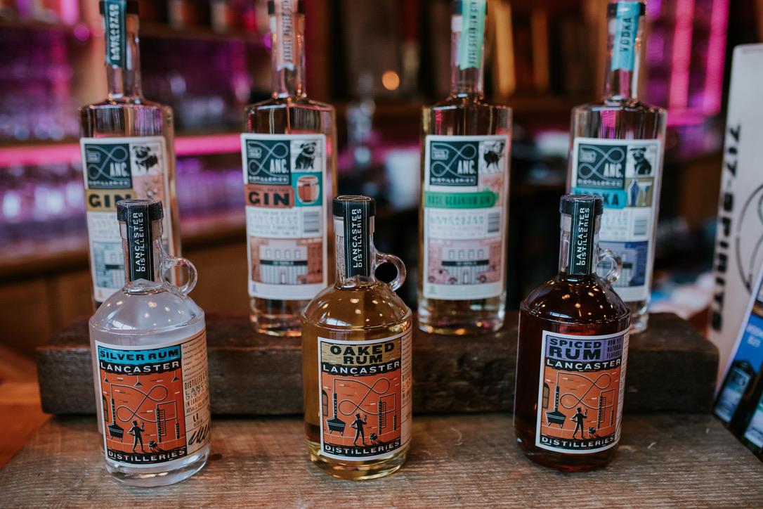 Six bottles of alcohol on a wooden surface with colorful blurred background, three in front and three behind, labels visible.