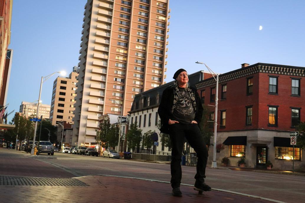 Person standing on a city street corner with tall buildings in the background during daytime.