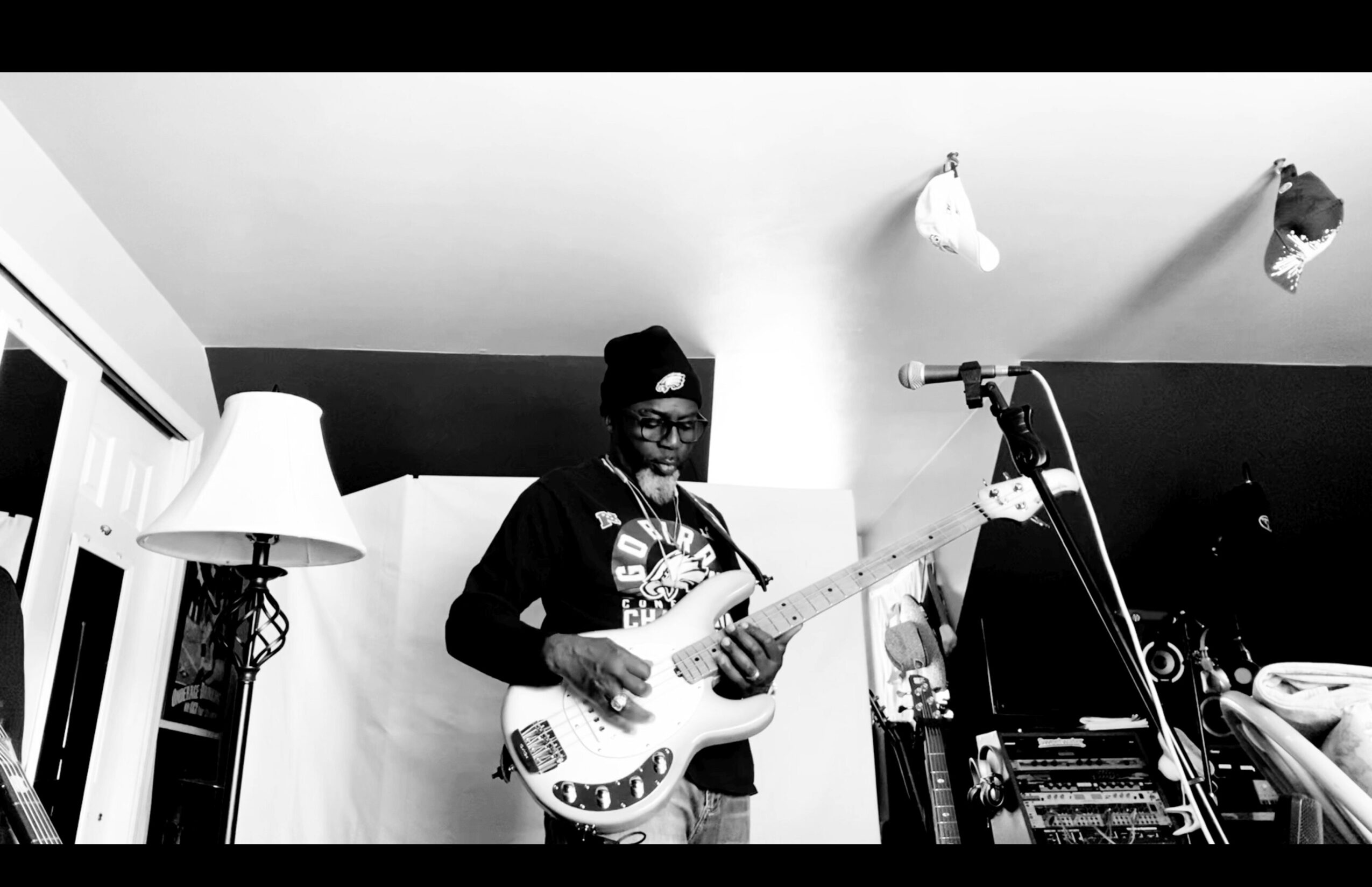 Person playing electric guitar in a room with a lamp and microphone, black and white photo.