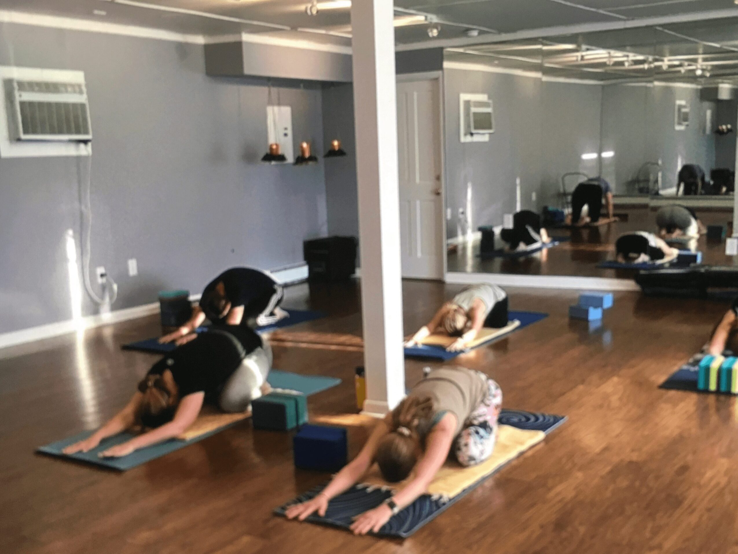 People practicing yoga on mats in a spacious, well-lit room with mirrors and wooden floors.
