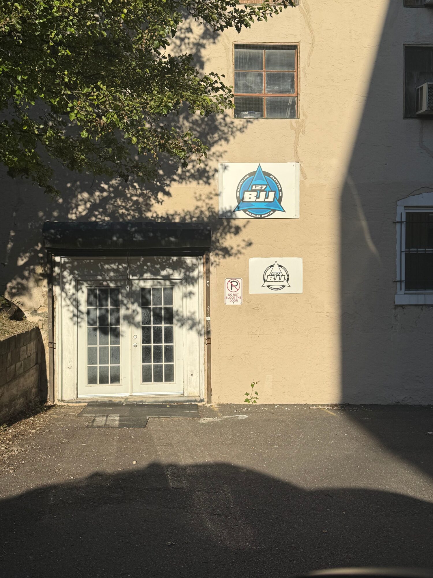 Building with windows, door, and signs, shadow of tree, and part of street, viewed from the side.