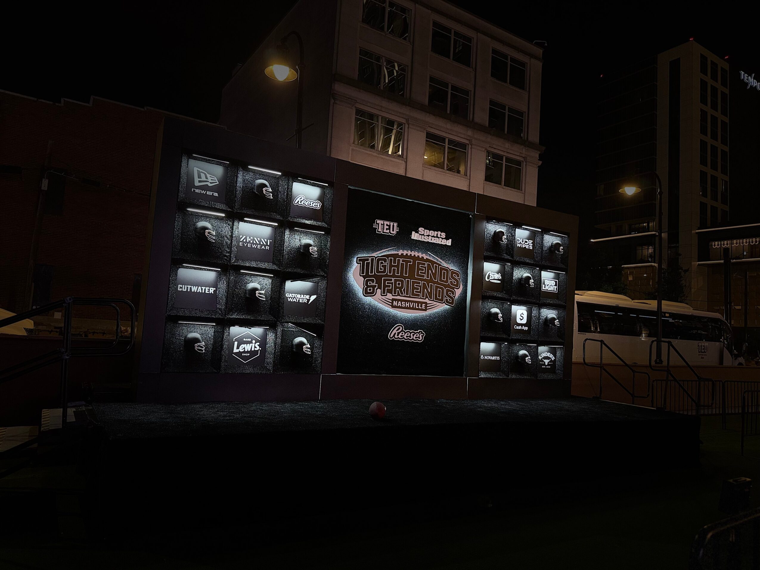 Nighttime outdoor display with multiple screens showing a logo and text, in an urban setting with buildings and streetlights.