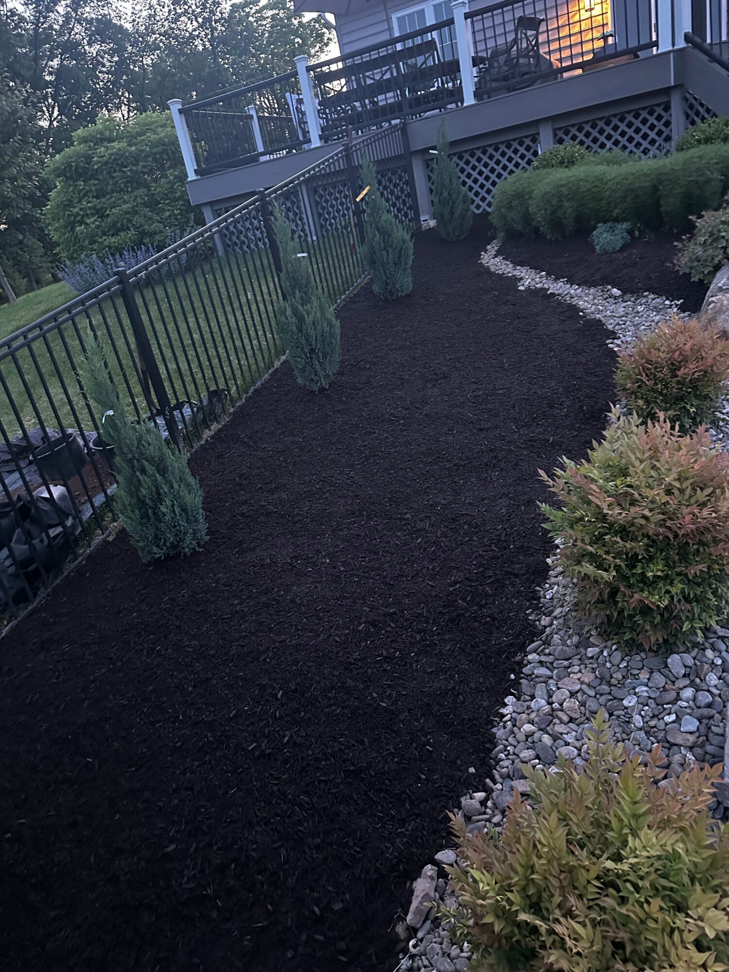 Garden pathway with freshly laid black gravel, bordered by plants and a metal fence, viewed from the side.