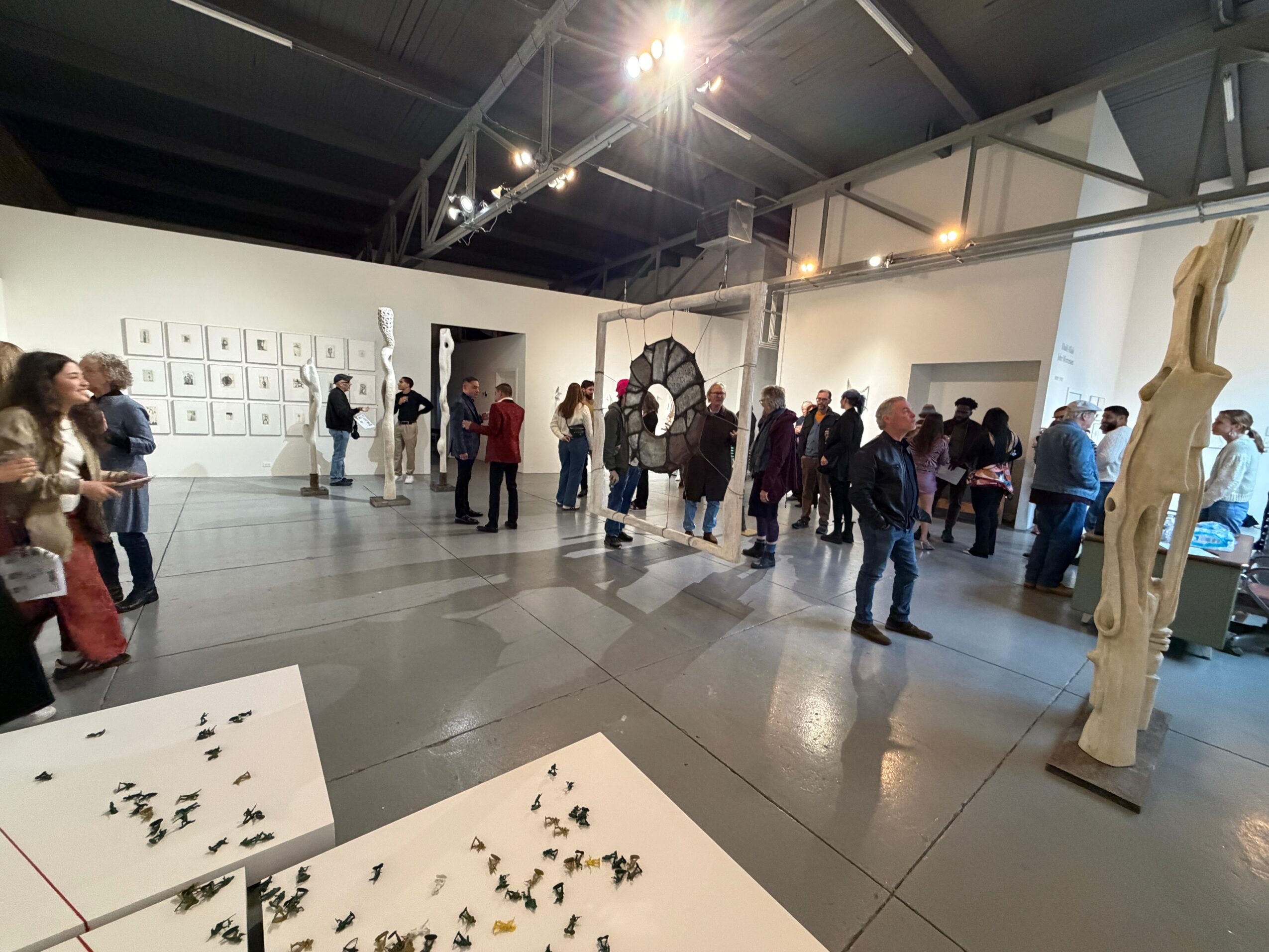 People viewing art exhibits in a spacious gallery with white walls and sculptures, some gathered around displays and artworks.