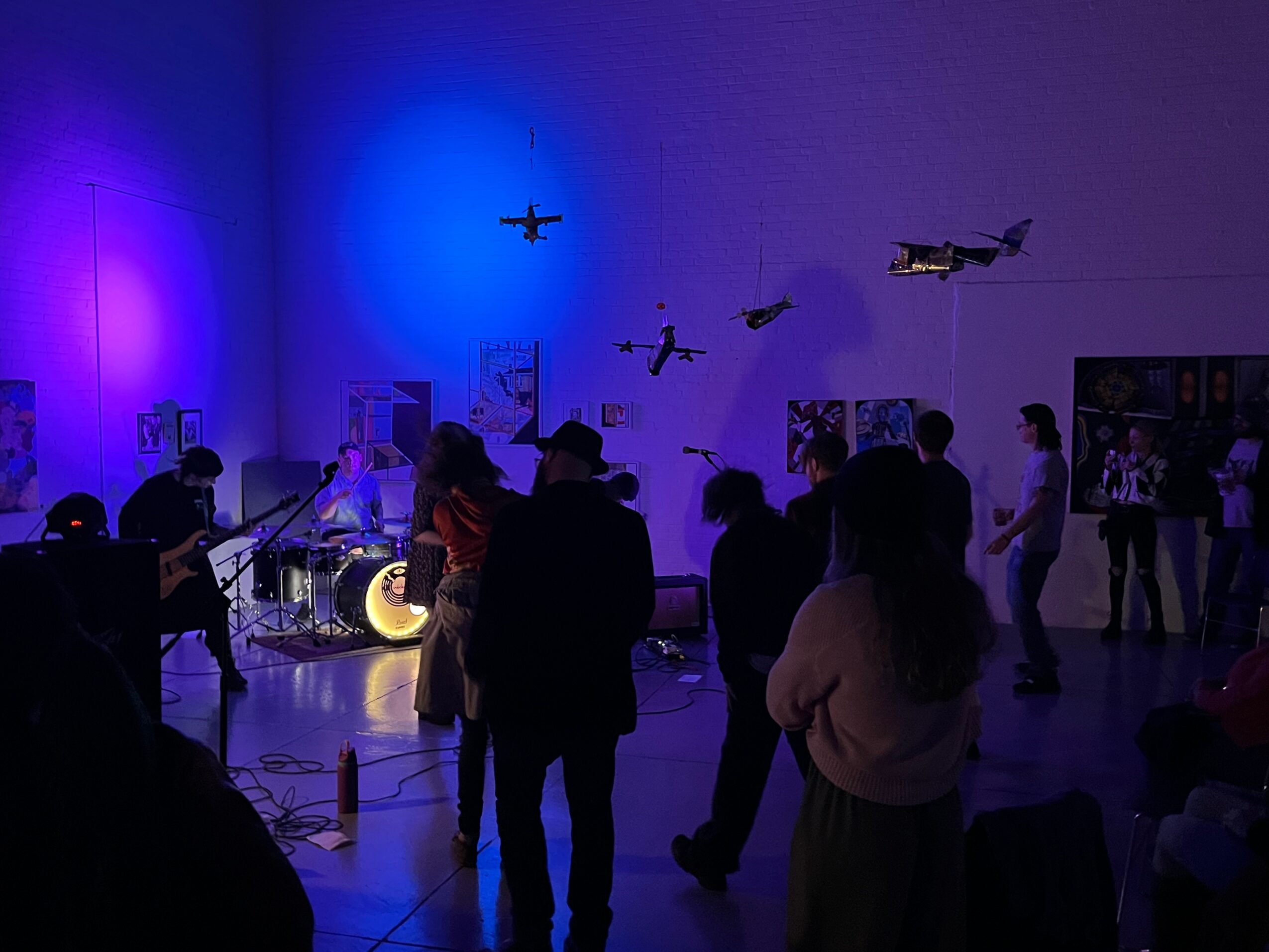 People in a dimly lit room with blue and purple lighting, observing aircraft models and displays on the wall.
