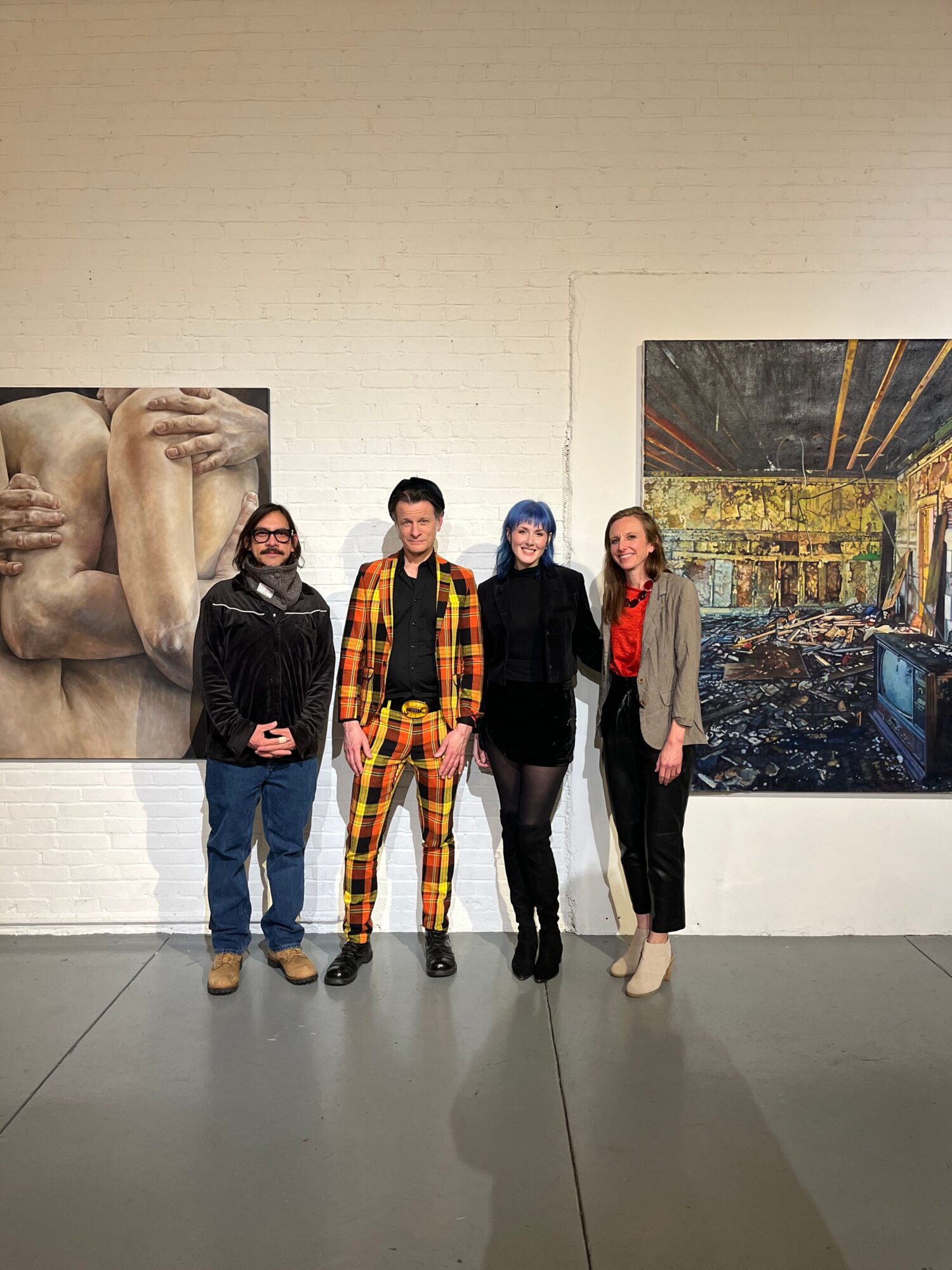 Four people standing in an art gallery with a large painting on the wall behind them.