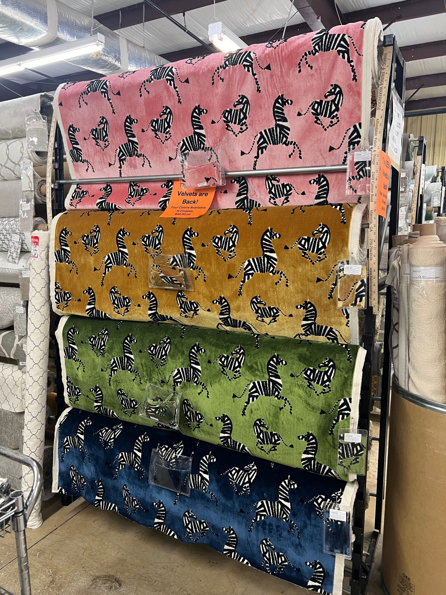 Four fabric rolls with zebra patterns in pink, yellow, green, and blue, standing upright on a shelf.