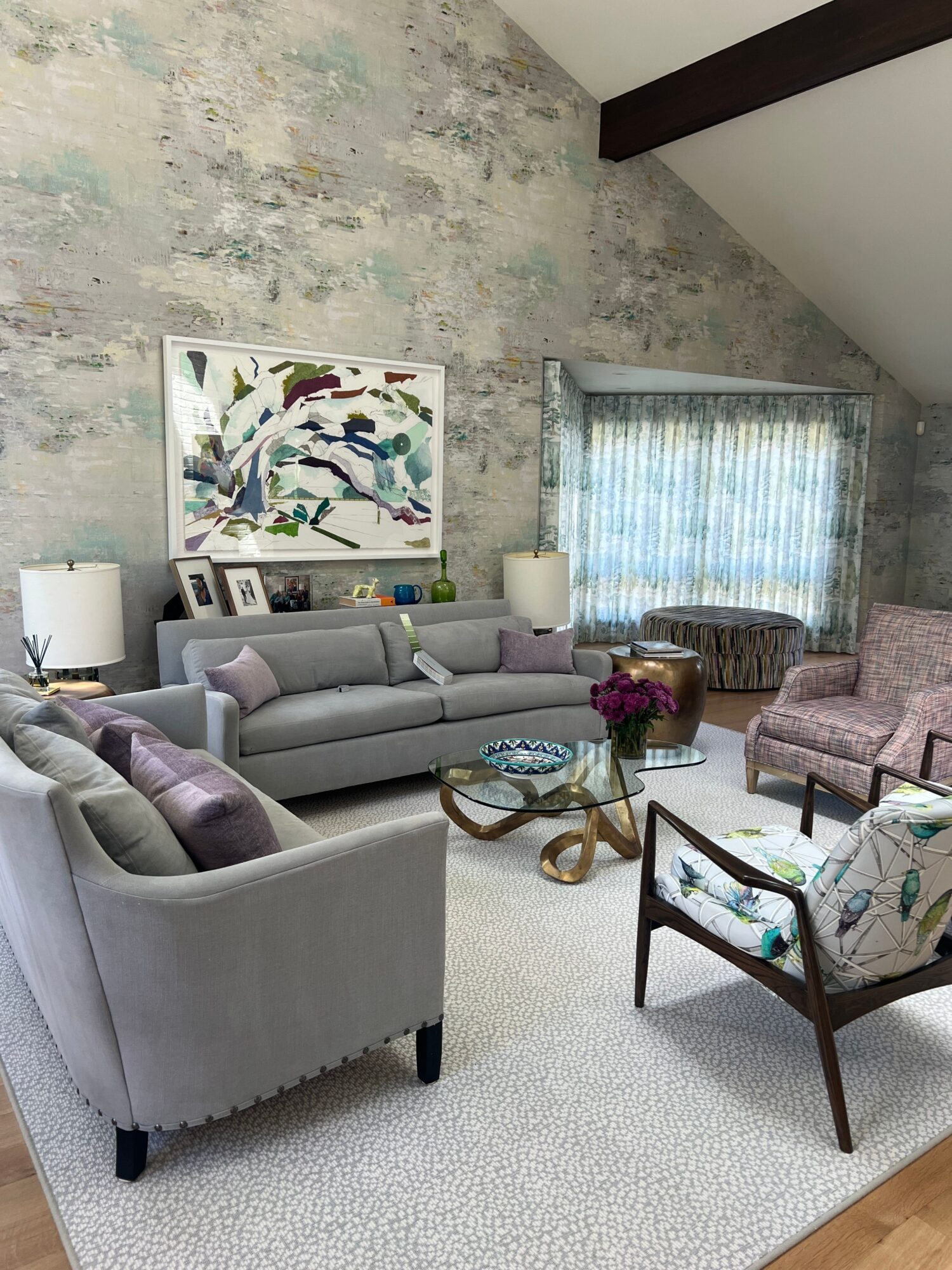 Living room with a gray sofa, armchair, coffee table, and artwork on the wall, with a window and curtains in the background.