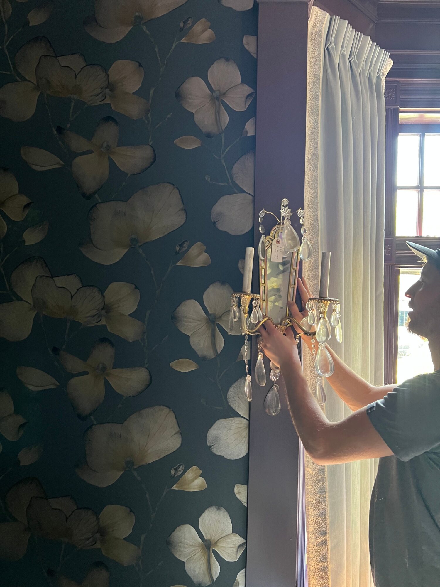 Person cleaning a windowsill with a cloth, curtains and window visible in the background.