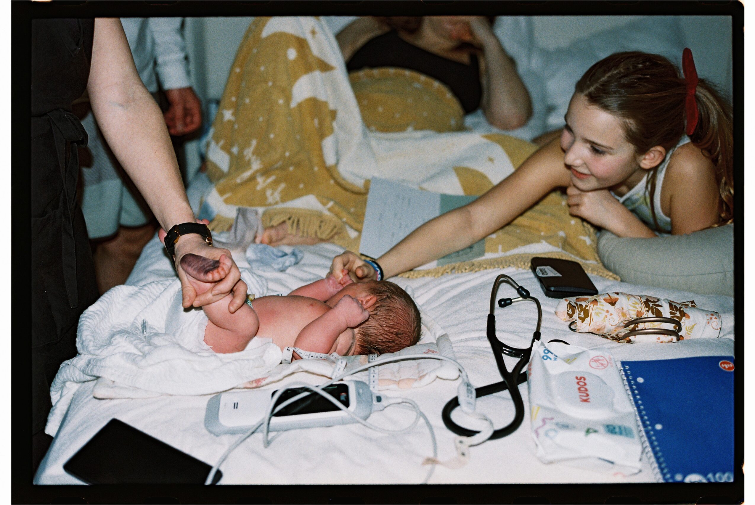 Young girl reaching out to touch a newborn baby lying on a hospital bed.