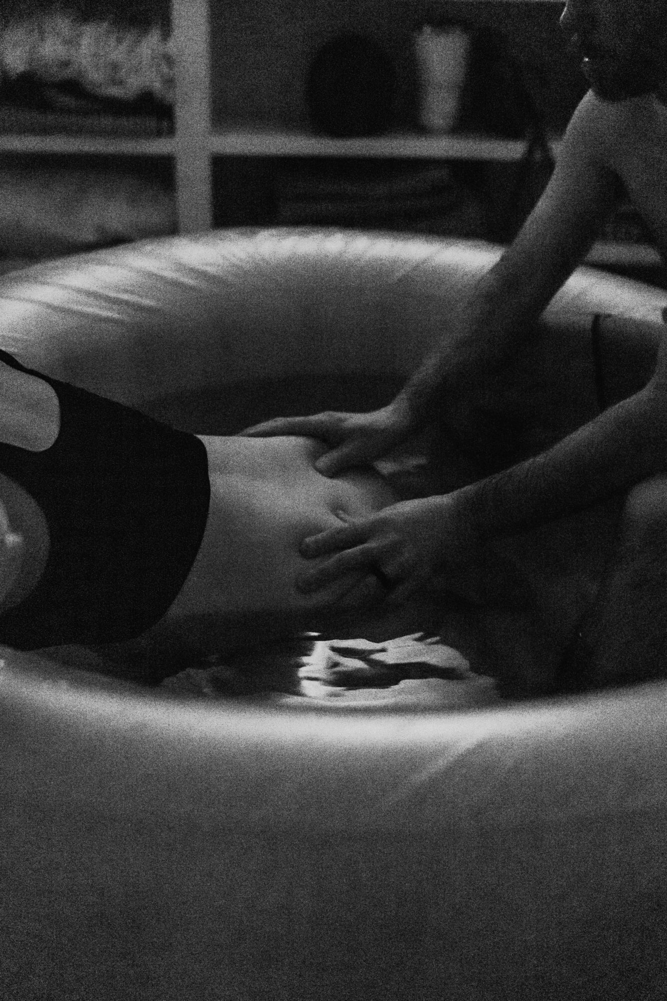 Two people hold hands over a small inflatable pool, with shelves and objects in the background.