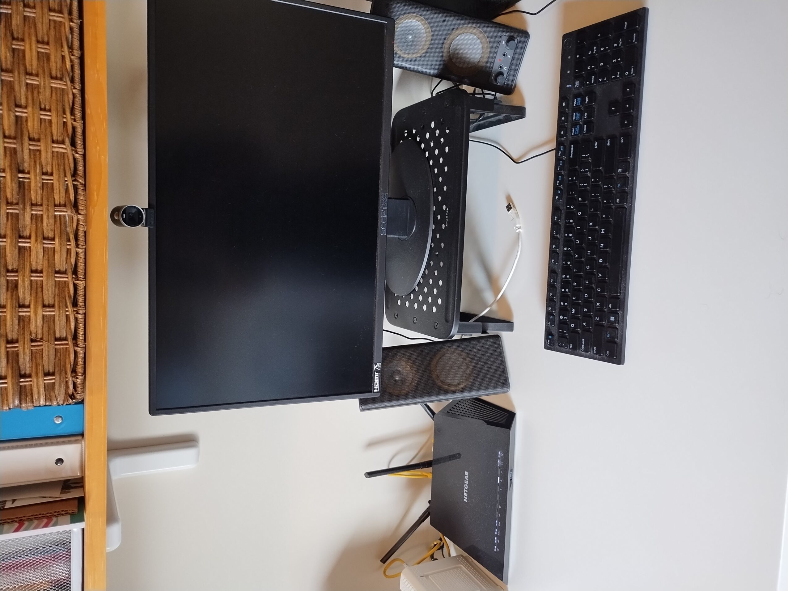 Computer monitor, speakers, keyboard, and other electronic devices on a desk, with a white wall in the background.