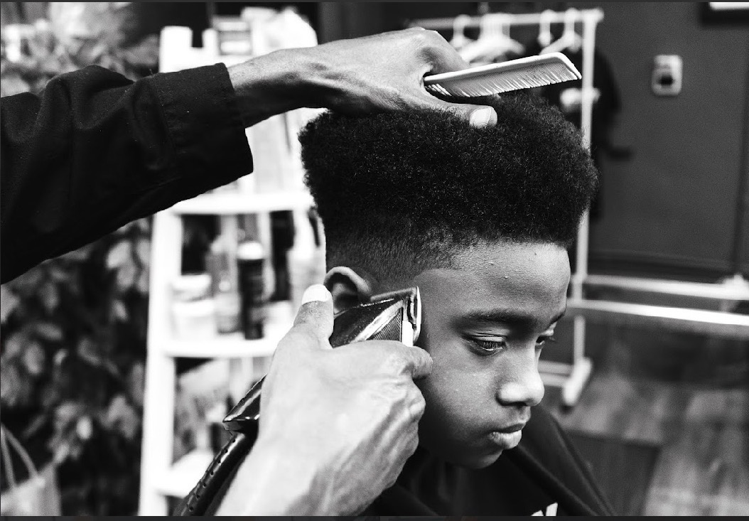 A person getting a haircut, with a barber using scissors and a comb on a young man's hair, in a barbershop.