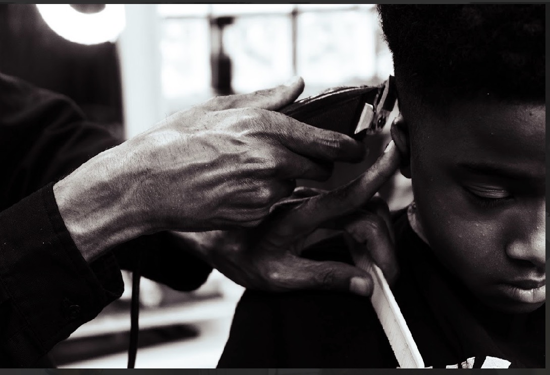 A person getting a haircut, with a barber using scissors near a child's head, in black and white.