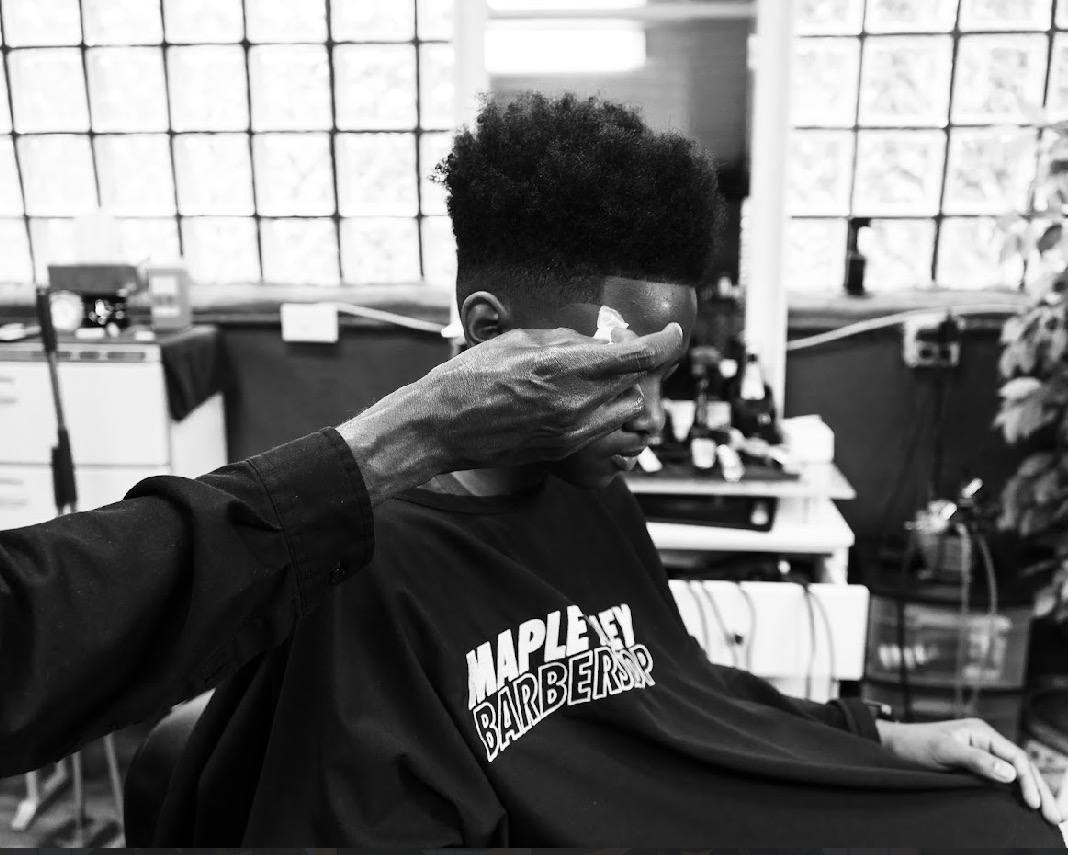 Person getting a haircut in a barbershop, with barber's hand on their face, black and white photo.