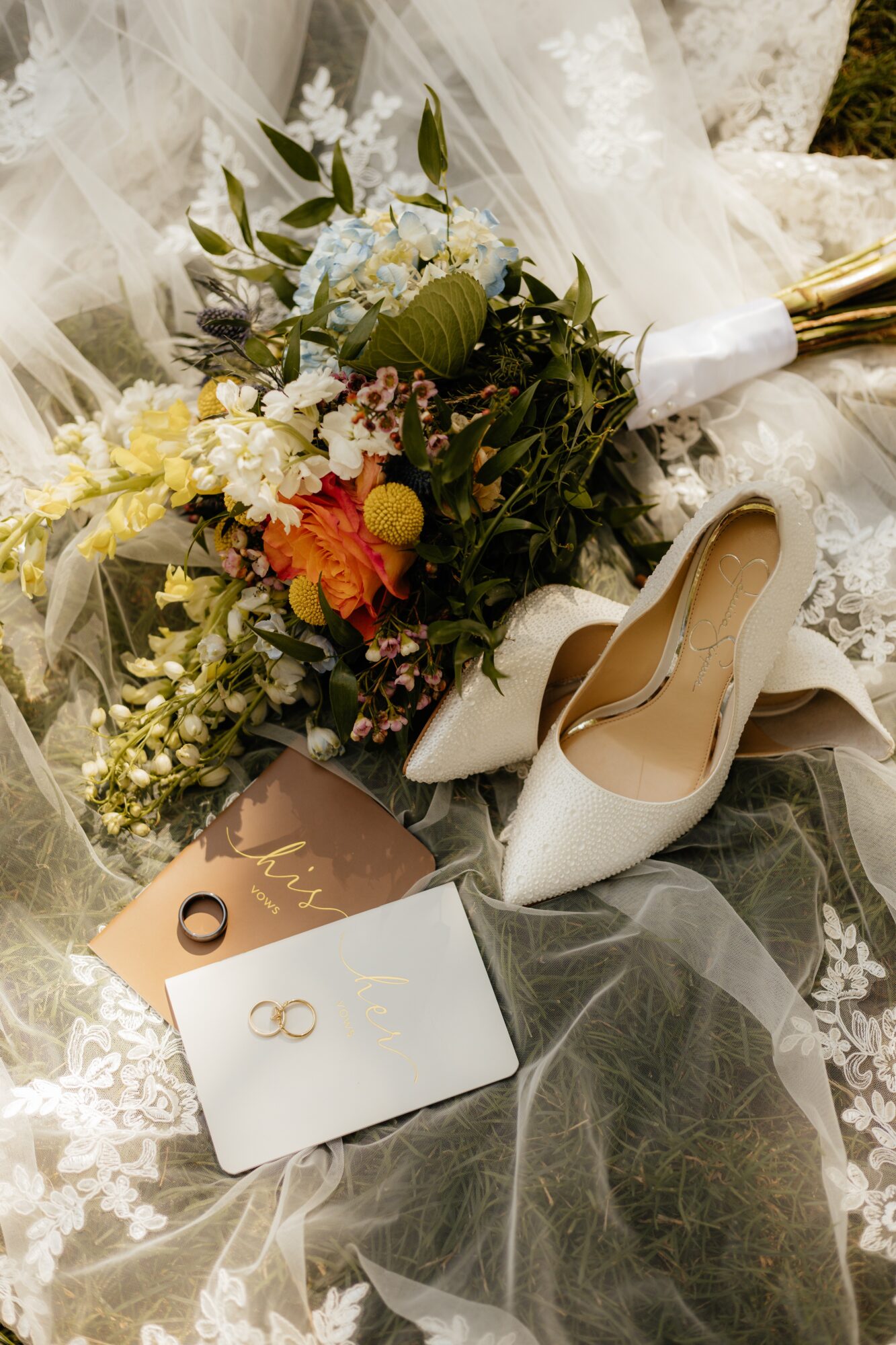 Wedding bouquet with flowers, white high heels, and wedding rings on lace fabric.