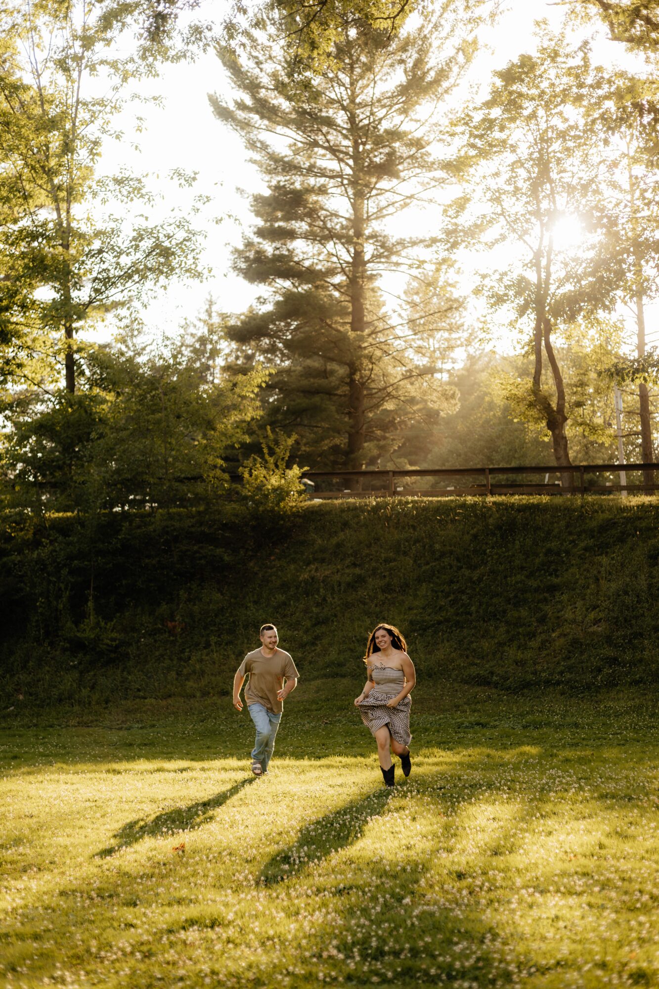 Two people walking on a grassy field with trees and sunlight in the background.